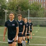 Jogadoras de futebol treinam em um campo durante o dia.