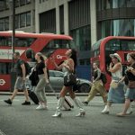 Pedestres atravessam uma rua de Londres enquanto ônibus vermelhos circulam ao fundo
