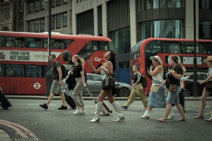 Pedestres atravessam uma rua de Londres enquanto ônibus vermelhos circulam ao fundo